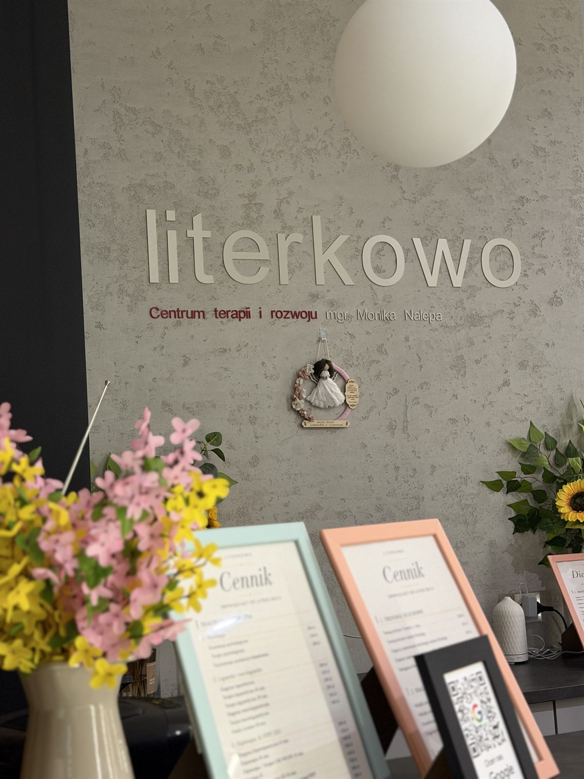 Recepcja poradni Literkowo — logo na ścianie, kwiaty i ramki z cennikiem
